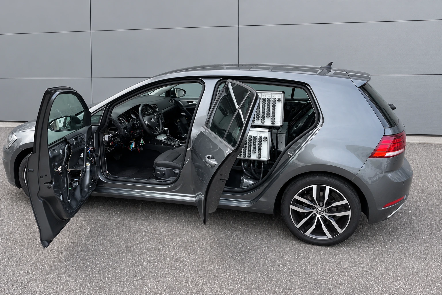 VW Golf Schulungsfahrzeug mit geöffneten Türen und integrierter Messtechnik vor grauer Hallenwand